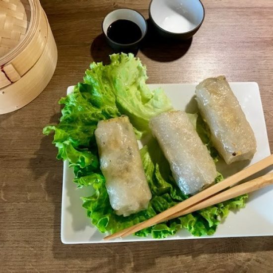 nems de poulet salade verte sur une assiette blanche rectangulaire et baguettes asiatiques